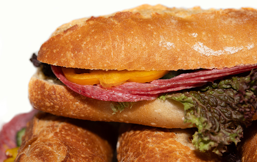 Close-up of a roll made from wheat flour, topped with slices of salami and lettuce. The bread is stacked on top of others.