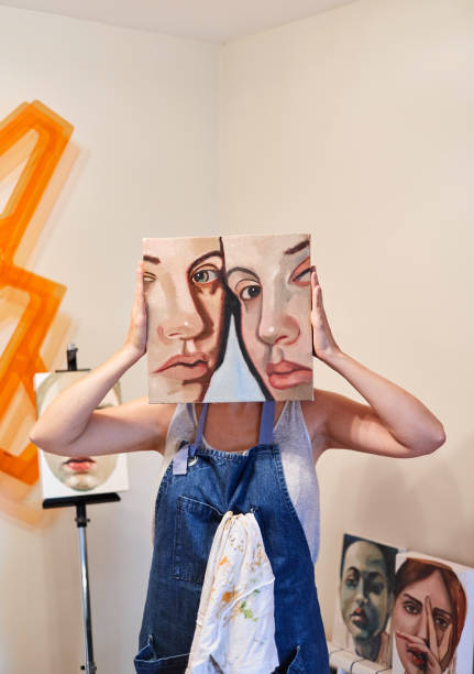 Woman artist showing her work of art in her home studio. Portrait of a female painter with her artwork on her face. Vertical photo abstract oil painting for beginners stock pictures, royalty-free photos & images