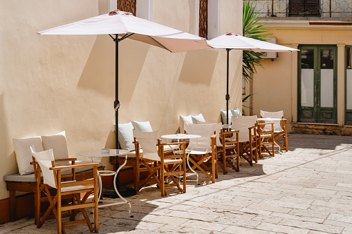 Sun-drenched cafe terrace with white umbrellas and wooden chairs offers a peaceful retreat in a Mediterranean setting