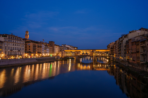 Historic Ponte Vecchio Bridge over the Arno River in Florence Italy at Night with Bright Lights and Calm Water