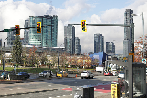 Surrey, Canada - December 8, 2023: Traffic goes along King George Boulevard near Holland Commons. TransLink passengers wait at the bus stop outside the SkyTrain King George Station. Background shows the green SFU at Central City tower and other downtown buildings near Surrey City Hall in Metro Vancouver.