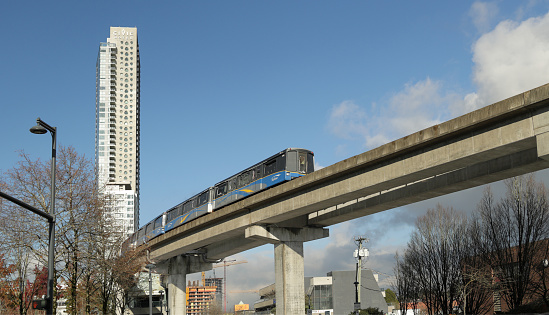 Surrey, Canada - December 8, 2023: A southbound SkyTrain leaves Surrey Central Station on the Expo Line. View from City Parkway at 102nd Avenue. Autumn afternoon with light clouds above Metro Vancouver.