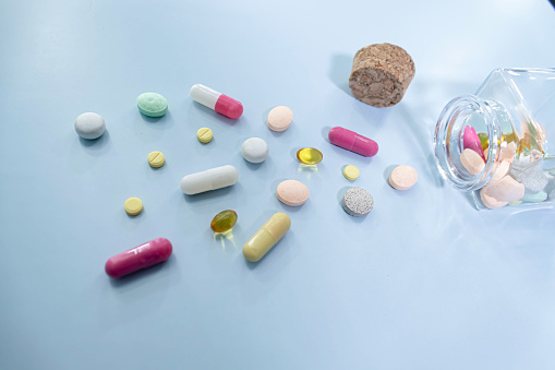 A medicine concept of an upturned jar full of medicines, drugs, tablets and pills spilling out onto a blue background with copy space.