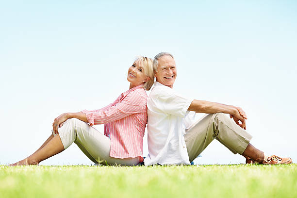 Elderly man sitting on a beanbag and reading a book with an elderly woman sitting on a beanbag and drinking from a cup isolated on white background