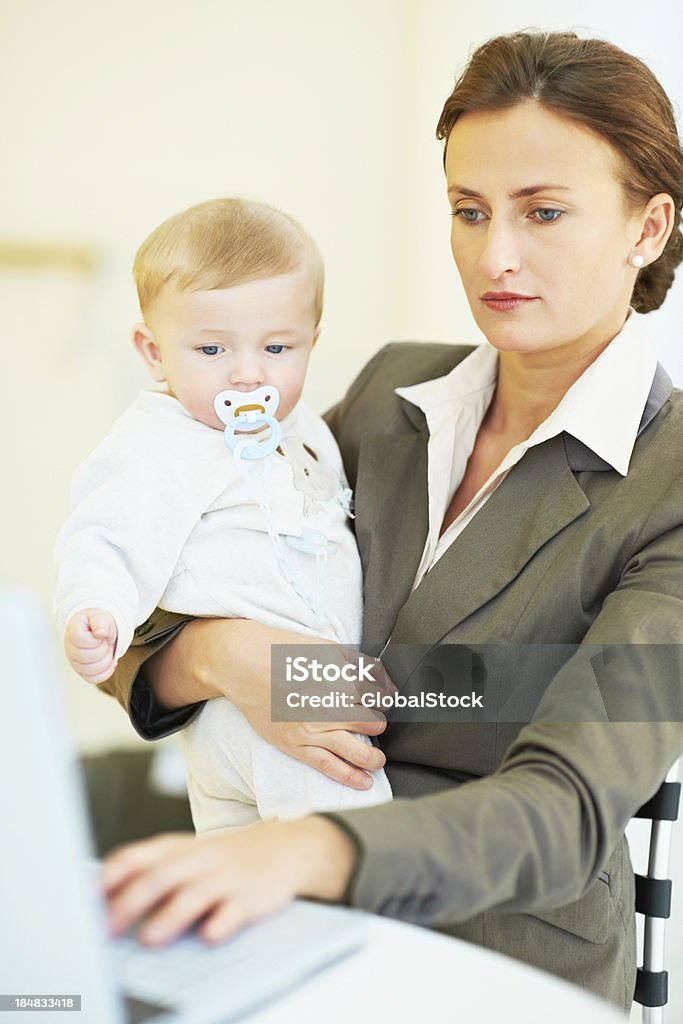 Working mother Portrait of a business mother working on her laptop holding child Adult Stock Photo