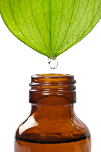 A fresh tropical leaf with a drop of water above a glass bottle isolated on white background.