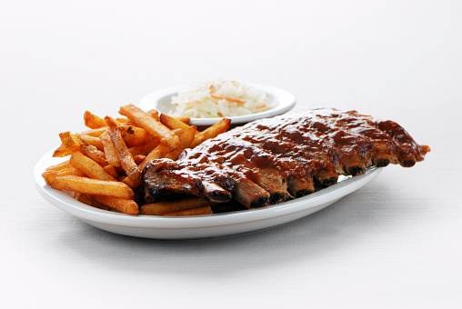 Plate of juicy barbecue ribs with spicy french fries and a side of coleslaw on a white background