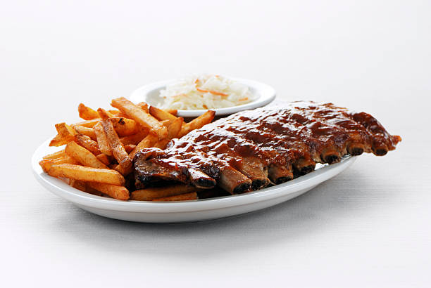Barbecue ribs and fries Plate of juicy barbecue ribs with spicy french fries and a side of coleslaw on a white background barbecue pork stock pictures, royalty-free photos & images