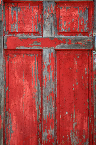 Old red wooden door with scratched and missing pint with cross design. Vertical image would be good for Christian or religious use.