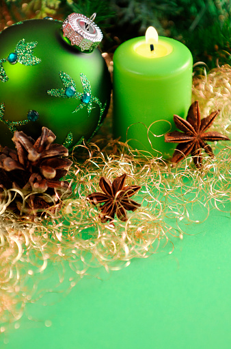 green Christmas ornament and burning candle standing on green paper background. Golden angel hair pasta with star anise. In background green pine twig and cone. Useful Copy space christmas background for greeting card.