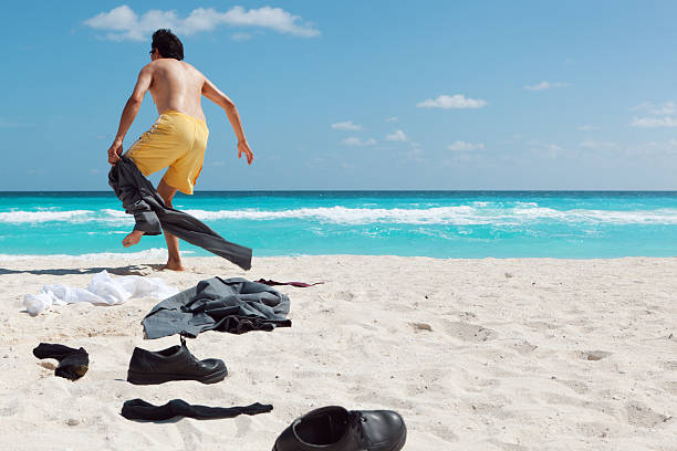 Desperate Businessman Needing a Vacation in Caribbean Beach Hz "Subject: An Asian businessman taking off his business attire running toward the sea, excited about a relaxing beach vacation.Location: Caribbean sea, Cancun, Riviera Maya, Mexico." undressing stock pictures, royalty-free photos & images