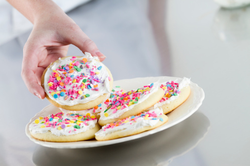 A hand reaching for a decorated sugar cookie on a plate.