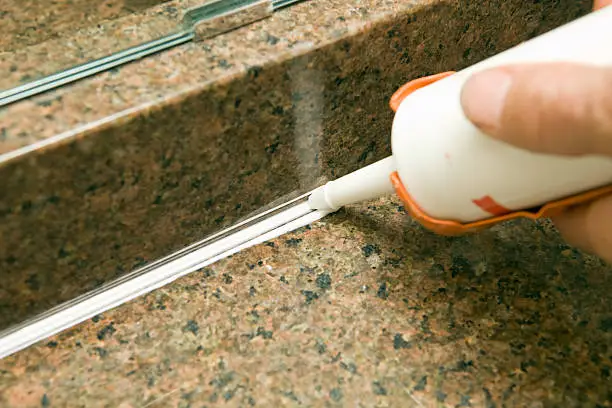 Photo of Caulk Gun Applying Silicone to Granite Sink Backsplash