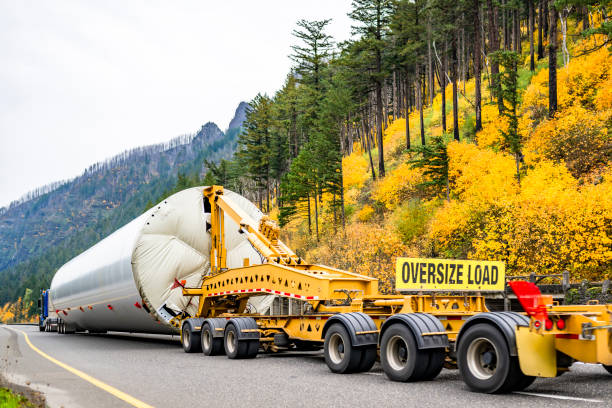 istock Blue big rig semi truck transporting oversized part of the wind generator support pole using an additional heavy duty trolley with six axles and oversize load sign driving on the autumn highway road 1848365595