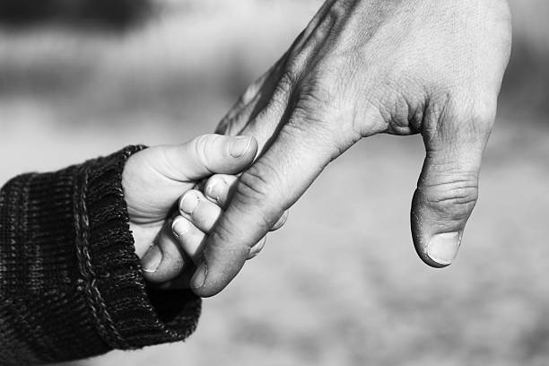 Father and Child Holding Hands A close up image of a child's small hand holding his father's hand. Black and white mage with some graininess. kid holding fathers hand stock pictures, royalty-free photos & images