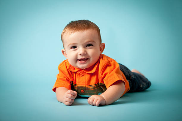 Color image of a happy six-month-old baby boy smiling while lying on blue background.