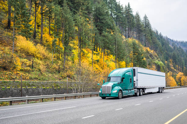 istock Light green bonnet big rig American semi truck tractor transporting cargo in refrigerator semi trailer driving on the multiline highway road with autumn yellow forest on the rock mountain hillside 1848377890