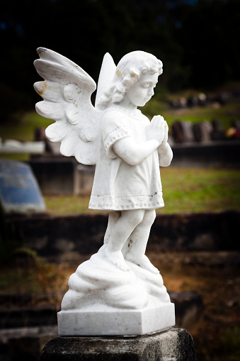 White marble statue of praying little girl angel at the cemetery, full frame vertical composition with vignette