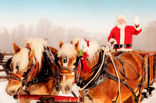 Waving Santa With Sleigh and Team of Horses in winter scene.  Two horses in red and green holiday trim.  The background is a foggy winter day.  Brrr, it is cold outside.  Santa is happy, jovial and waving to the viewer.  Copy space.