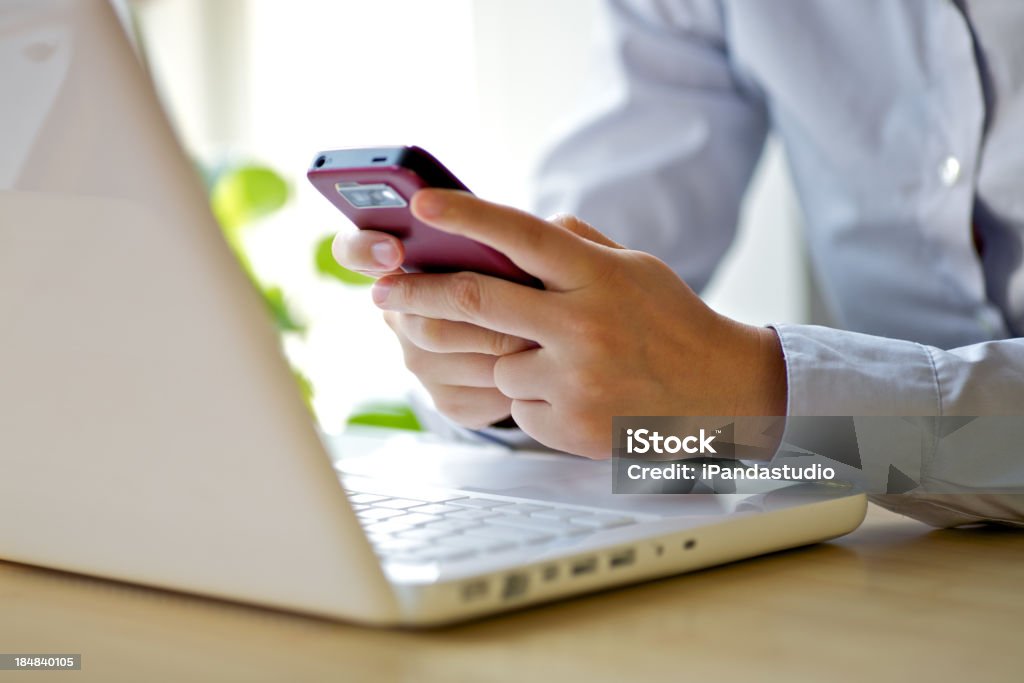 A businesswoman using her smartphone and laptop texting with the cellphone Adult Stock Photo