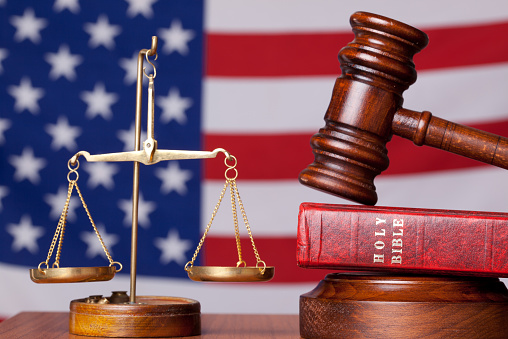 Bible, gavel and scales of justice on american flag background.The focus in on the objects.The flag background is blurred.Bible is placed under the gavel.Horizontal frame, shot with a full frame DSLR camera.