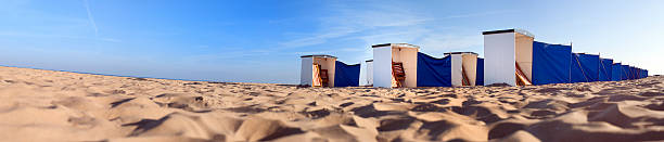 low angle panorama view on rows of colorful empty beach huts at the North Sea coast at dawn in The Netherlands on a sunny day