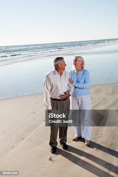 Coppia Senior In Piedi Sulla Spiaggia - Fotografie stock e altre immagini di 60-69 anni - 60-69 anni, 65-69 anni, Abbigliamento casual