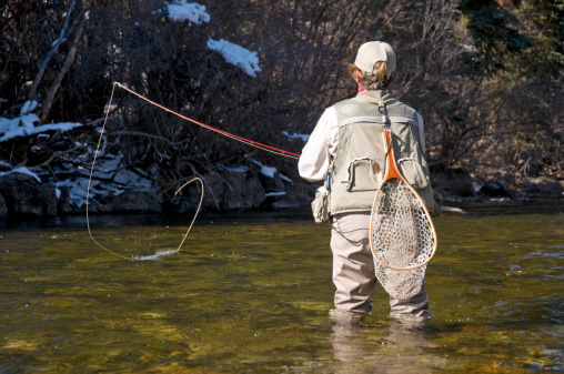 A woman mends her line while fly-fishing in a mountain river during the fall.