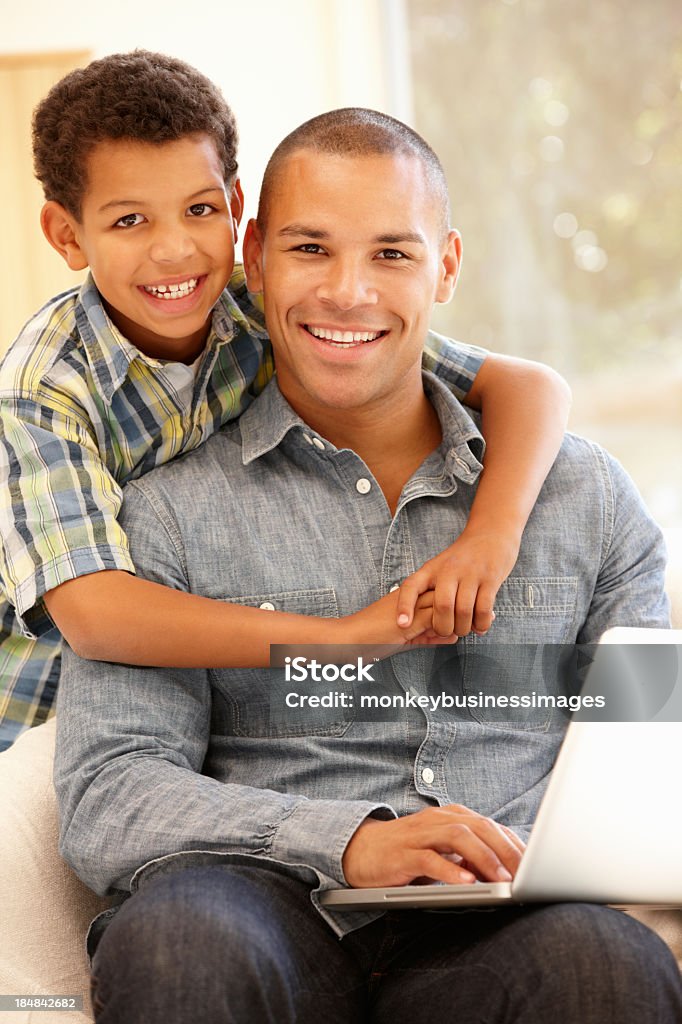 Hombre trabajando en portátil en casa con hijo - Foto de stock de 10-11 años libre de derechos