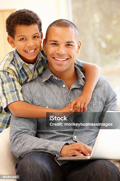 Hombre Trabajando En Portátil En Casa Con Hijo Foto de stock y más banco de imágenes de 10-11 años - 10-11 años, 30-39 años, Adulto