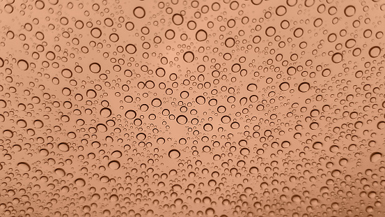 Abstract image of rain drops on glass. Image toned in peach color. New Fashion color. Top view. Abstract drops view