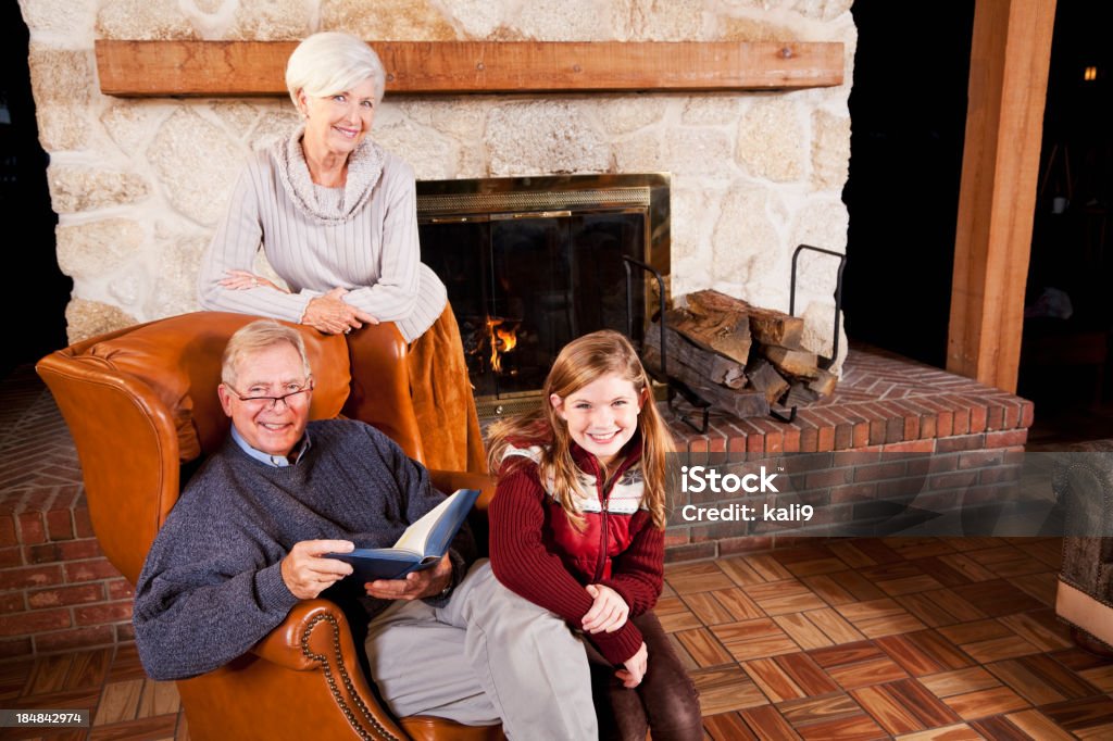 Menina e avós leitura ao lado da lareira - Foto de stock de Inverno royalty-free