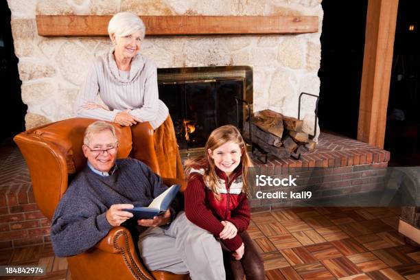 Foto de Menina E Avós Leitura Ao Lado Da Lareira e mais fotos de stock de Inverno - Inverno, Aconchegante, Família