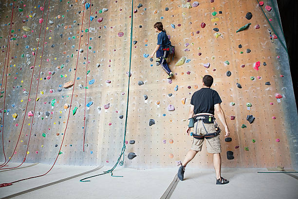 10 year old boy climbing on a rock climbing wall while an adult is supervising