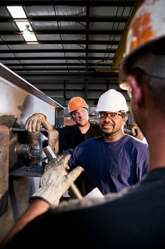 Multiracial industrial workers working in factory, wearing hard hat and safety goggles.