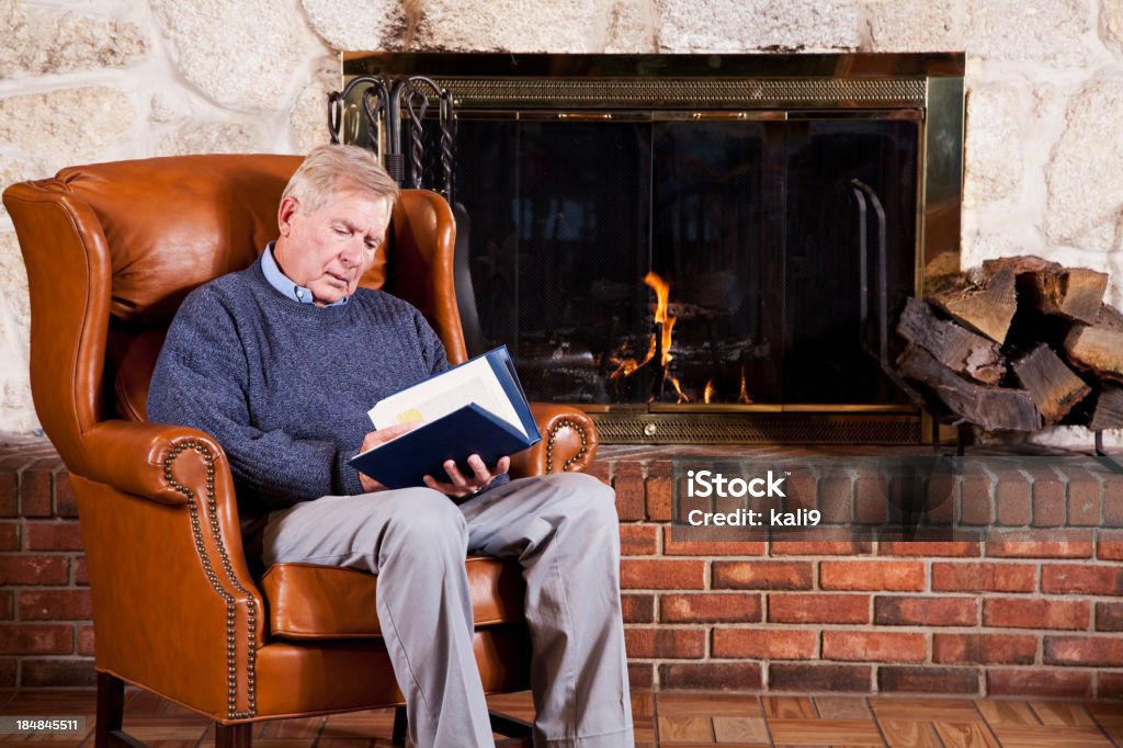 Hombre mayor lectura por chimenea - Foto de stock de Cabaña de madera libre de derechos