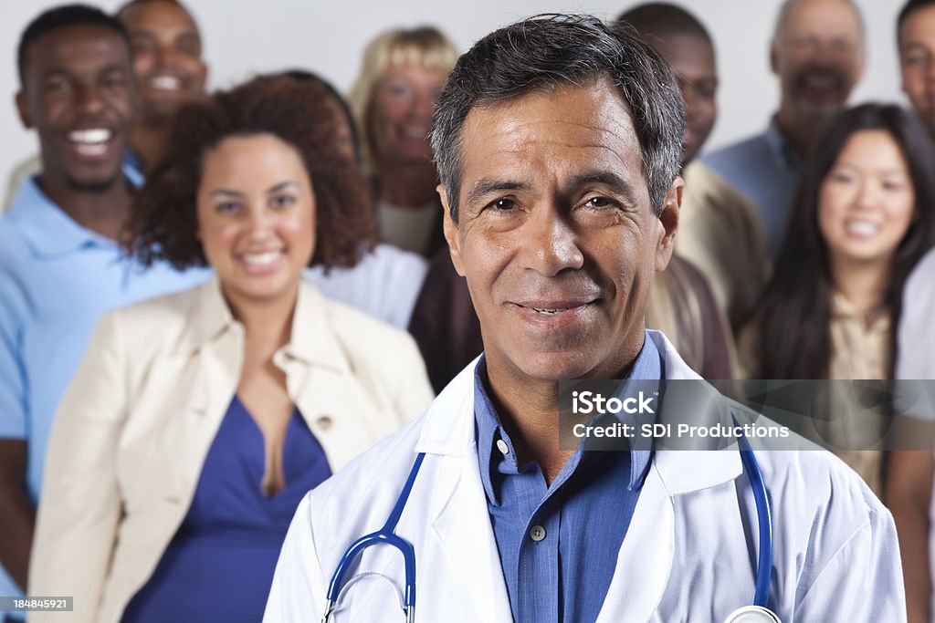 Happy experienced doctor in front, diverse group of patients "Happy experienced doctor in front, diverse group of patients." Doctor Stock Photo