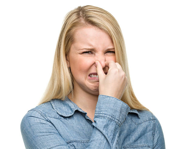 Grossed Out Young Woman Pinches Nose Portrait of a young woman on a white background. frowning headshot close up studio shot stock pictures, royalty-free photos & images