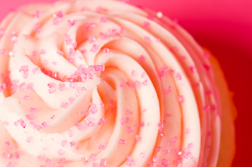 A closeup of an icing swirl with sprinkles on a pink background.