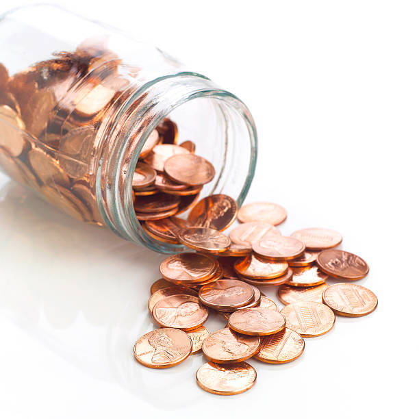 Jar of shiny US pennies spilling out on refective white stock photo