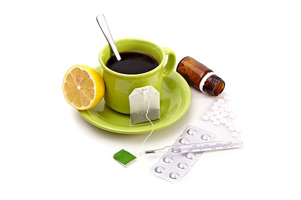 A green cup of tea with cut orange and medicine beside it stock photo