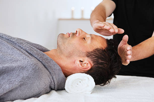 Man Receiving New Age Therapy New age practitioner directs energy towards a young man's head. Horizontal shot. reiki photos stock pictures, royalty-free photos & images