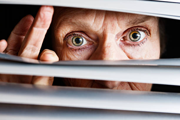 istock Concerned curious old woman looks through venetian blinds 184849487