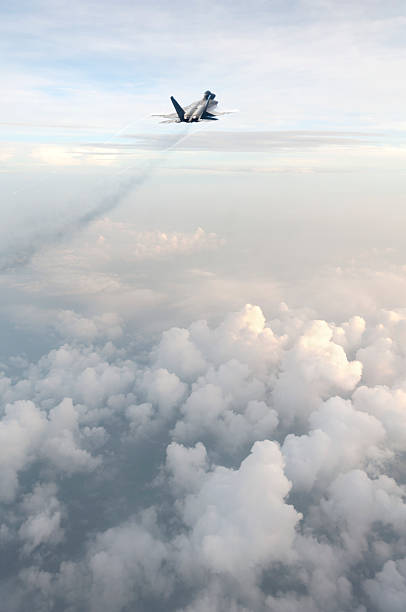 An F22 fighter jet soars above the clouds leaving vapor trails in it's wake.