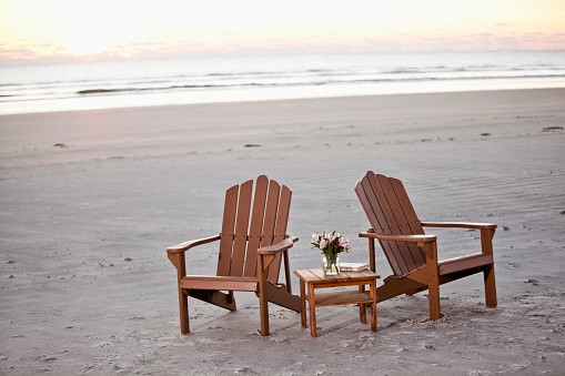 Two adirondack chairs on beach at sunrise.