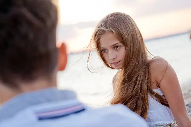"Pretty bored teenage girl with serious expression on her face looking away, thinking about something. In the foreground is the boy's back. Shallow DOF."