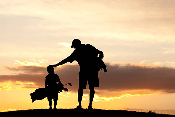 Junior Golfer With Father A junior golfer with his dad. Horizontal colour image. Silhouette. Golf concept. Additional themes in the image are sports, leisure, family, fun, mentor, coach, coaching, teaching, learning, junior level, son, boys, men, care, father, father's day, parenting, parent, single father, encourage, encouragement, love, relationships, and support. Boy is young and kindergarten age.  toddler hitting stock pictures, royalty-free photos & images