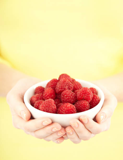 Close-up crop of woman holding a bowl containing raspberries