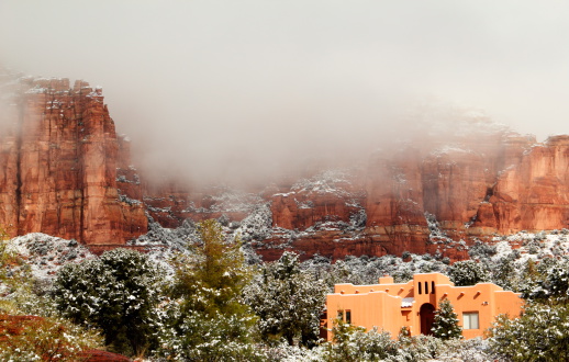 A winter scene of a southwestern house with a red rock backdrop.