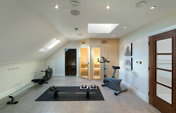 loft gym "A gym and sauna room in the loft of a luxury new home. Next to the sauna is a shower cubicle. Equipment includes an exercise bike, rowing machine and some free weights. Natural light is streaming in through two skylight windows. Photographer's own imagery on walls.Please see my other Interior and Architectural images by clicking on the Lightbox link below...A>AA>A" exercise room stock pictures, royalty-free photos & images